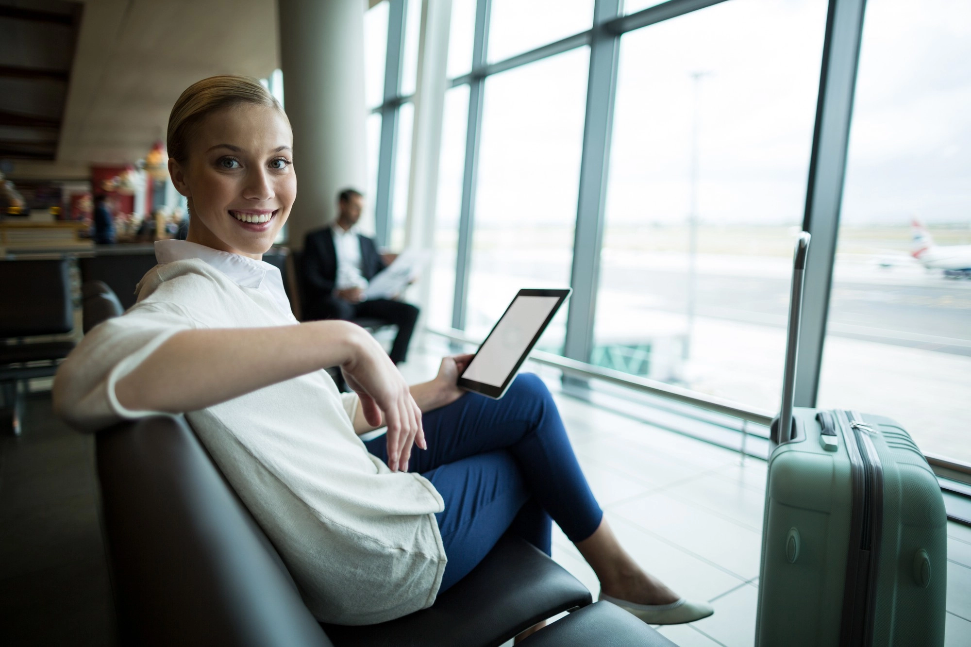 A traveler waiting at Venice Marco Polo Airport with a tablet and luggage, near the Titian Inn Hotel Venice Airport